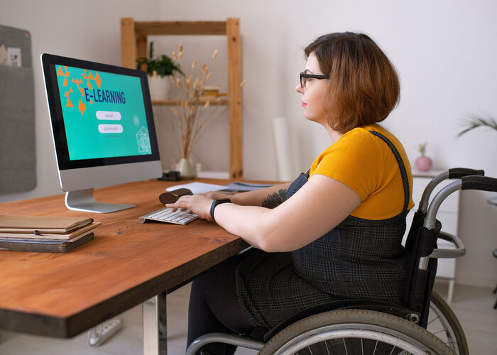 Frau im Rollstuhl am PC arbeitend an einem Schreibtisch